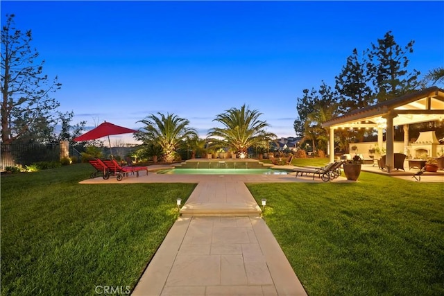 yard at dusk with a patio, an outdoor fireplace, fence, and an outdoor pool