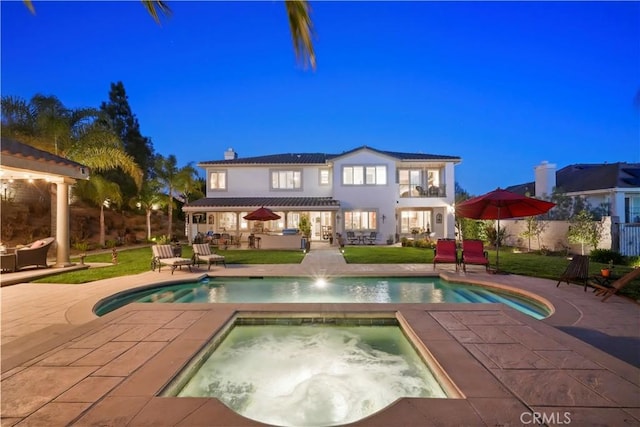 back of property with a chimney, a yard, a patio area, an outdoor pool, and an in ground hot tub