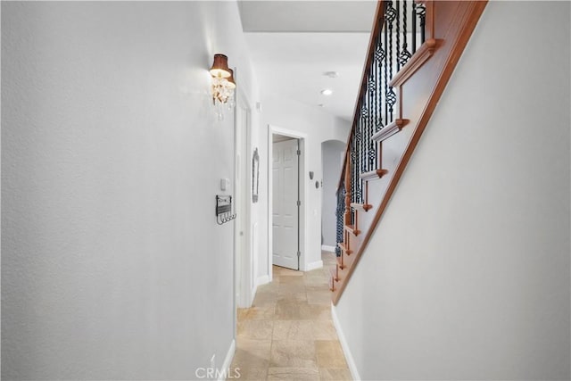 corridor with baseboards, arched walkways, and stairs