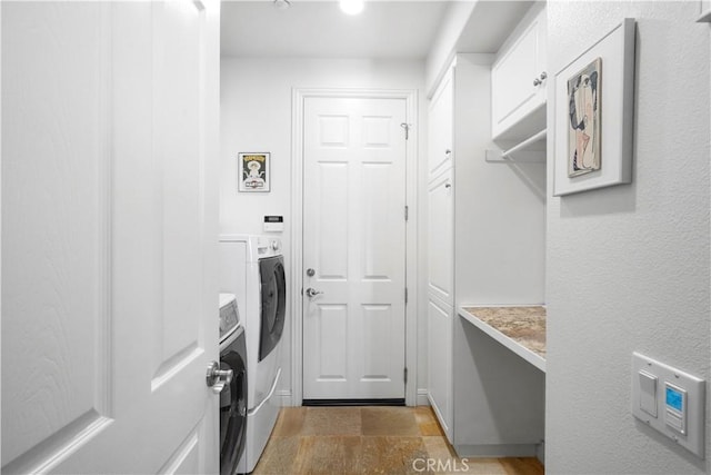 clothes washing area with washing machine and clothes dryer, cabinet space, and stone finish floor