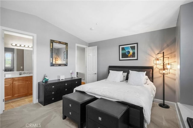 bedroom featuring ensuite bathroom, a sink, baseboards, light colored carpet, and vaulted ceiling