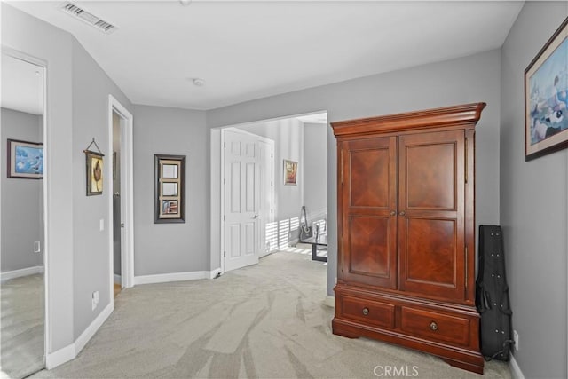 hallway with visible vents, light colored carpet, and baseboards