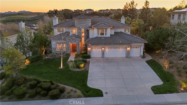 mediterranean / spanish home featuring driveway, a tile roof, stone siding, a yard, and a chimney