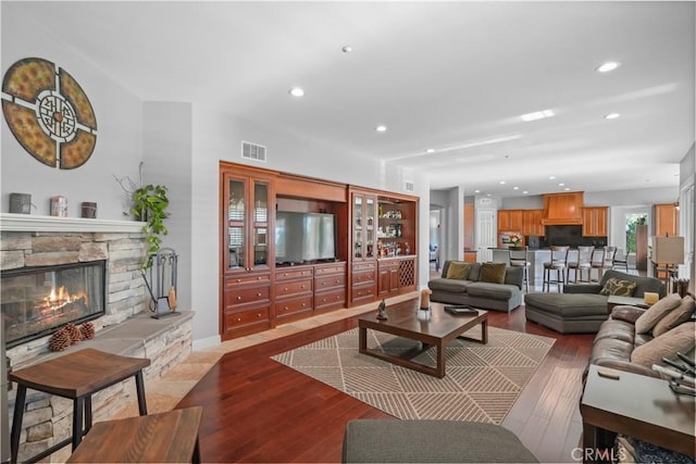 living area with a stone fireplace, wood finished floors, recessed lighting, and visible vents