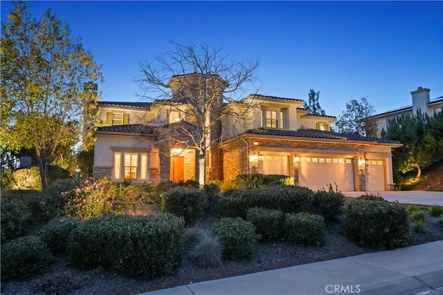 mediterranean / spanish-style home featuring a tile roof, stucco siding, a garage, stone siding, and driveway