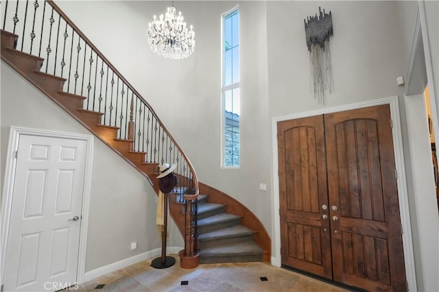 foyer entrance with stairs, a high ceiling, a notable chandelier, and baseboards