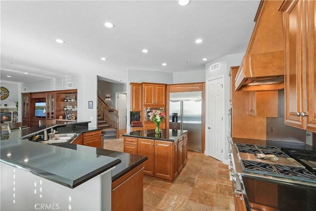 kitchen with a spacious island, custom range hood, appliances with stainless steel finishes, brown cabinetry, and a sink