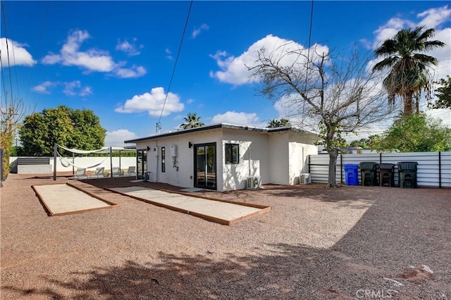 back of house featuring volleyball court, fence, and stucco siding