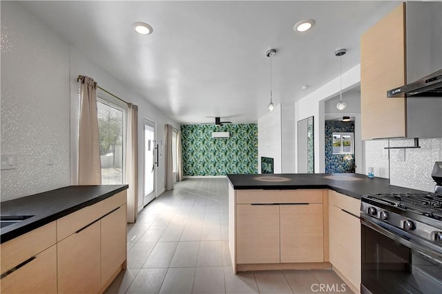 kitchen featuring a peninsula, stainless steel gas range, backsplash, dark countertops, and pendant lighting