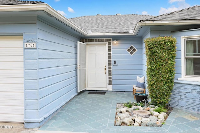 view of exterior entry with an attached garage and roof with shingles