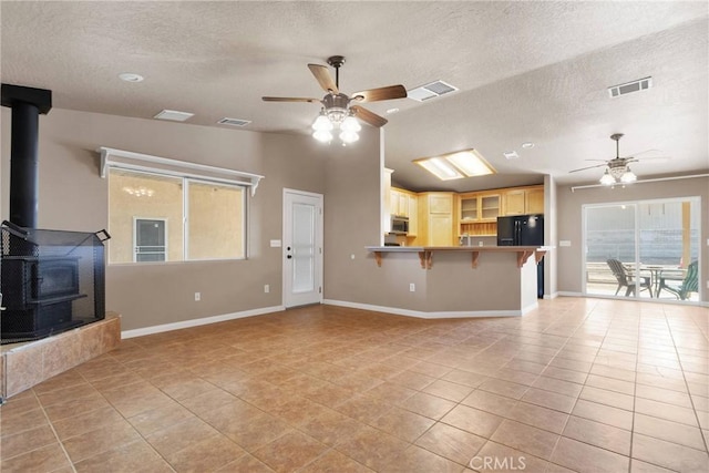 unfurnished living room with a wood stove, ceiling fan, visible vents, and light tile patterned flooring