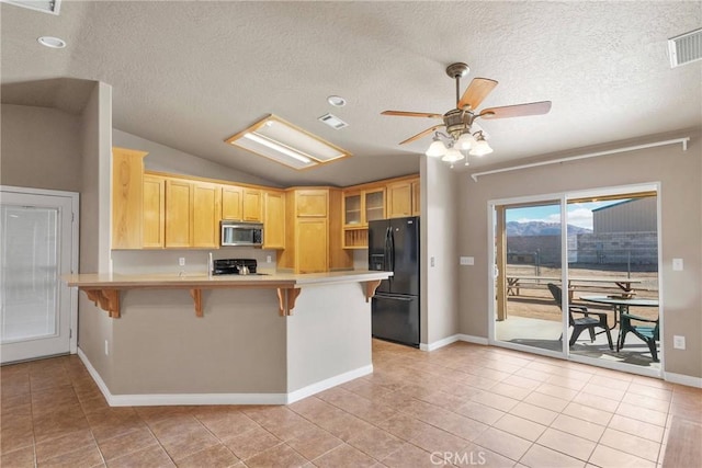 kitchen with a peninsula, a breakfast bar, visible vents, black refrigerator with ice dispenser, and stainless steel microwave