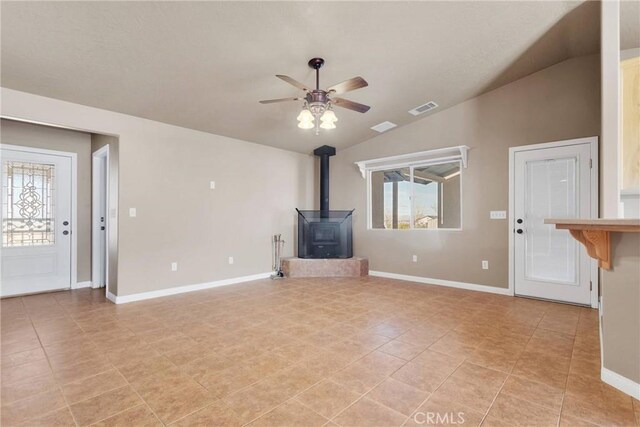 unfurnished living room with a wood stove, lofted ceiling, baseboards, visible vents, and ceiling fan