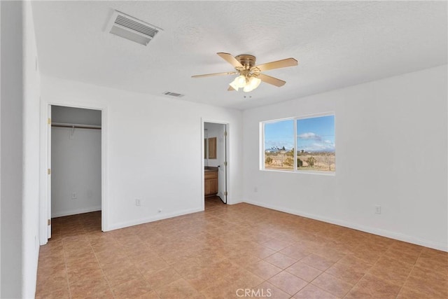 unfurnished bedroom featuring a walk in closet, visible vents, connected bathroom, and baseboards