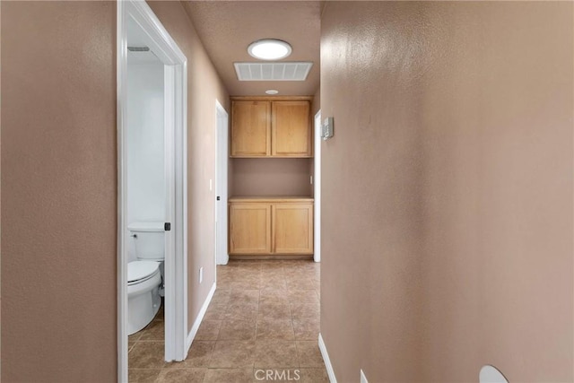 corridor with baseboards, visible vents, and light tile patterned flooring