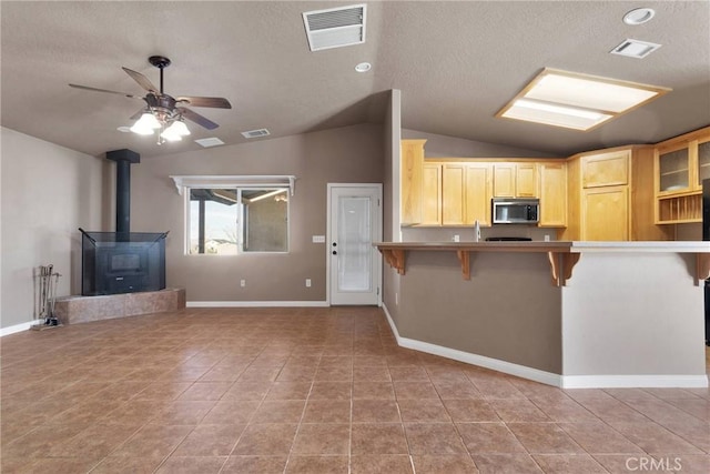 kitchen featuring a wood stove, stainless steel microwave, a breakfast bar area, and visible vents