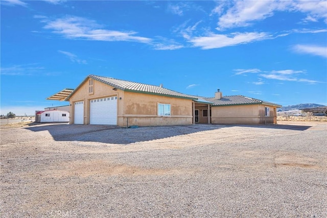 view of front facade with a chimney, stucco siding, an attached garage, and dirt driveway