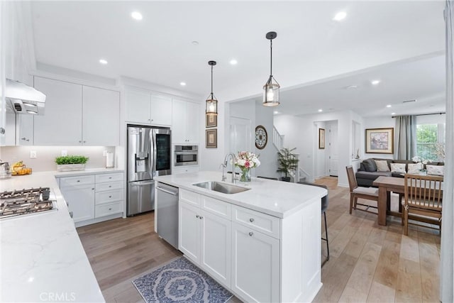 kitchen with a kitchen island with sink, light wood-style flooring, a sink, appliances with stainless steel finishes, and range hood