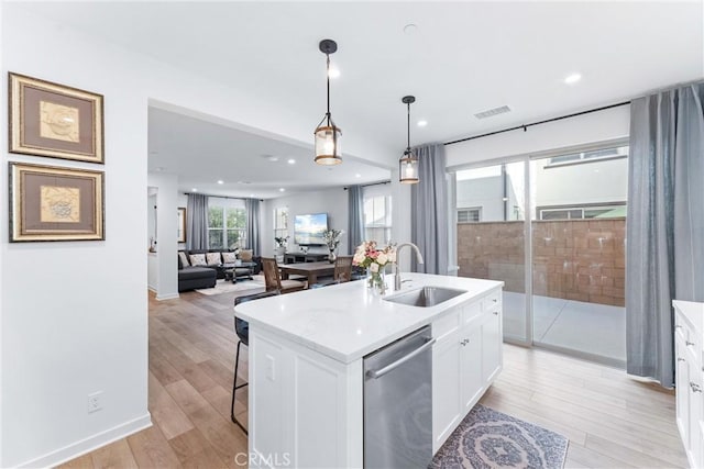 kitchen with a sink, white cabinets, light countertops, stainless steel dishwasher, and light wood finished floors