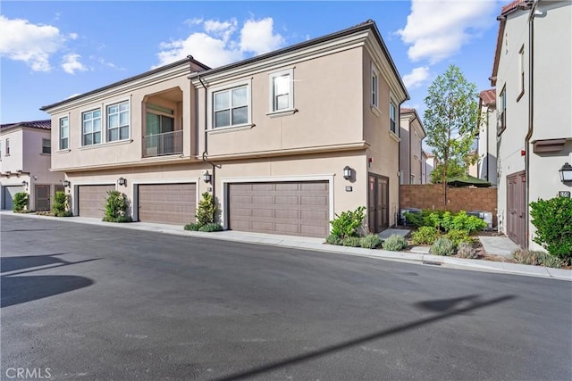 townhome / multi-family property featuring a residential view, fence, an attached garage, and stucco siding