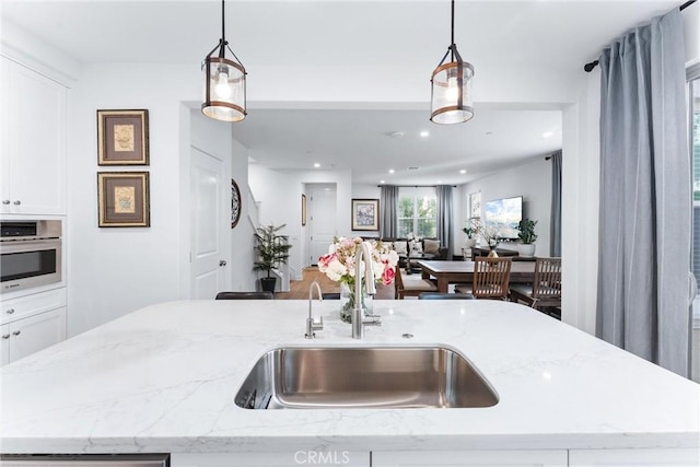 kitchen with light stone counters, white cabinets, a sink, and decorative light fixtures