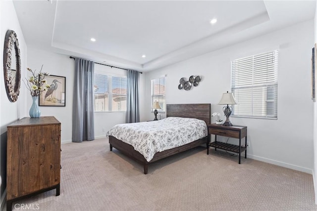 bedroom featuring baseboards, a raised ceiling, and light colored carpet