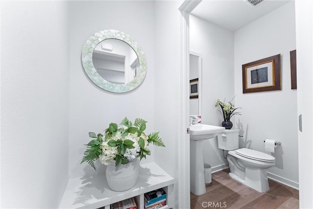 half bath featuring a sink, wood finished floors, toilet, and baseboards