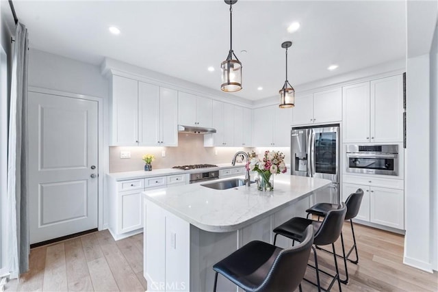 kitchen featuring under cabinet range hood, stainless steel appliances, a sink, white cabinetry, and light wood finished floors