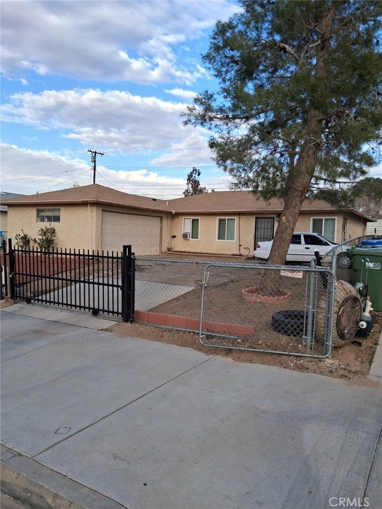 ranch-style house featuring a fenced front yard, an attached garage, driveway, a gate, and stucco siding