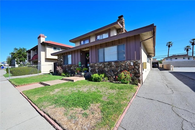 view of front facade with board and batten siding, stone siding, a chimney, and a front lawn