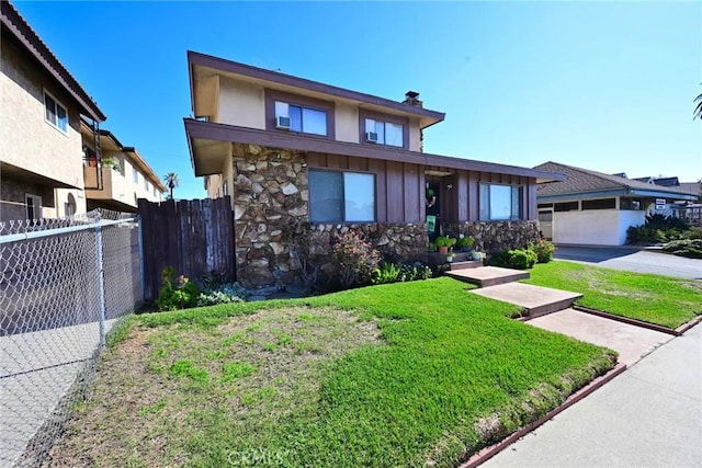 view of front of home featuring stone siding, fence, a front lawn, and board and batten siding