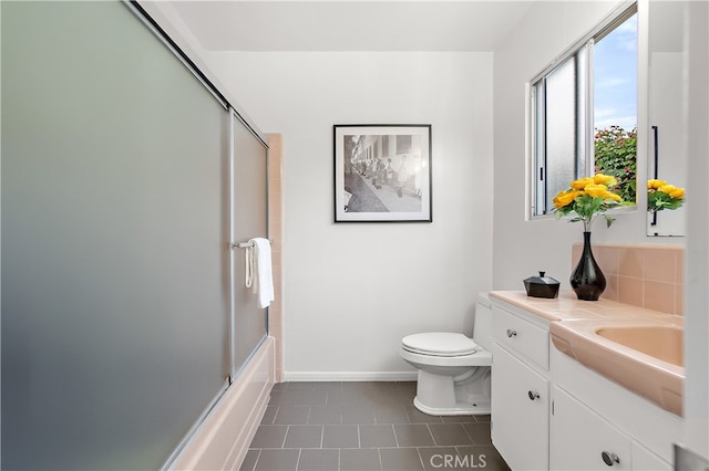 bathroom featuring toilet, enclosed tub / shower combo, vanity, baseboards, and tile patterned floors