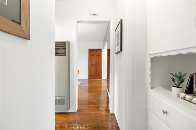 corridor featuring baseboards, a heating unit, and wood finished floors