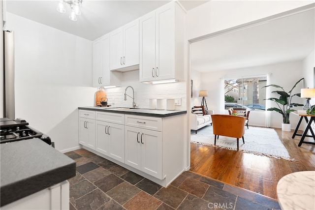 kitchen with tasteful backsplash, stone tile flooring, white cabinets, a sink, and baseboards