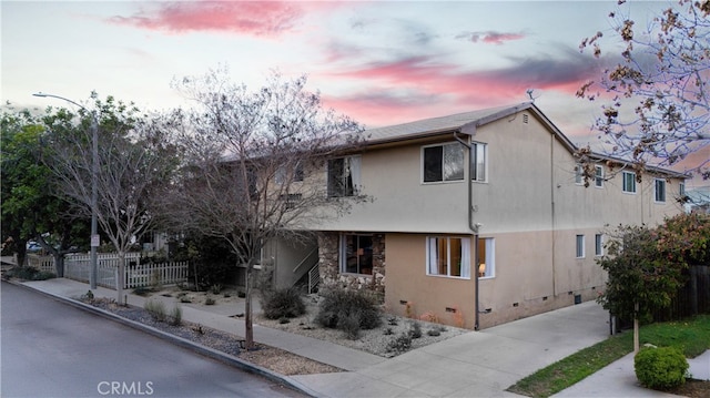 view of front of home featuring stone siding, crawl space, fence, and stucco siding