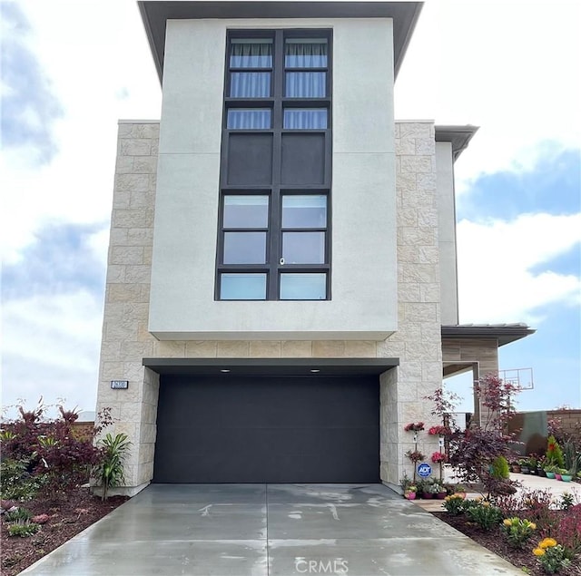 modern home featuring driveway, stone siding, an attached garage, and stucco siding