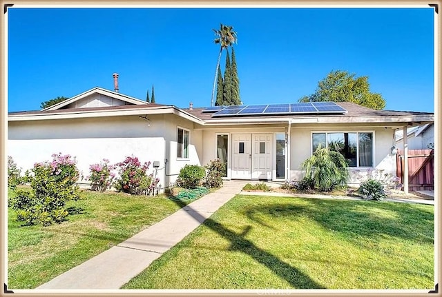 ranch-style home with a front yard, roof mounted solar panels, fence, and stucco siding