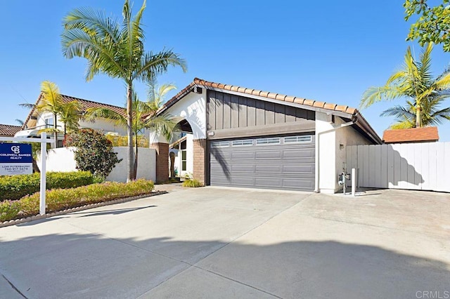 view of front of home with board and batten siding, concrete driveway, a garage, and fence