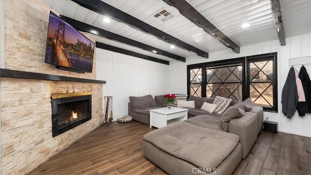 living room featuring beamed ceiling, a stone fireplace, wood finished floors, and visible vents