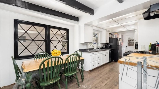 kitchen featuring white cabinetry, wall chimney range hood, beamed ceiling, wood finished floors, and black appliances