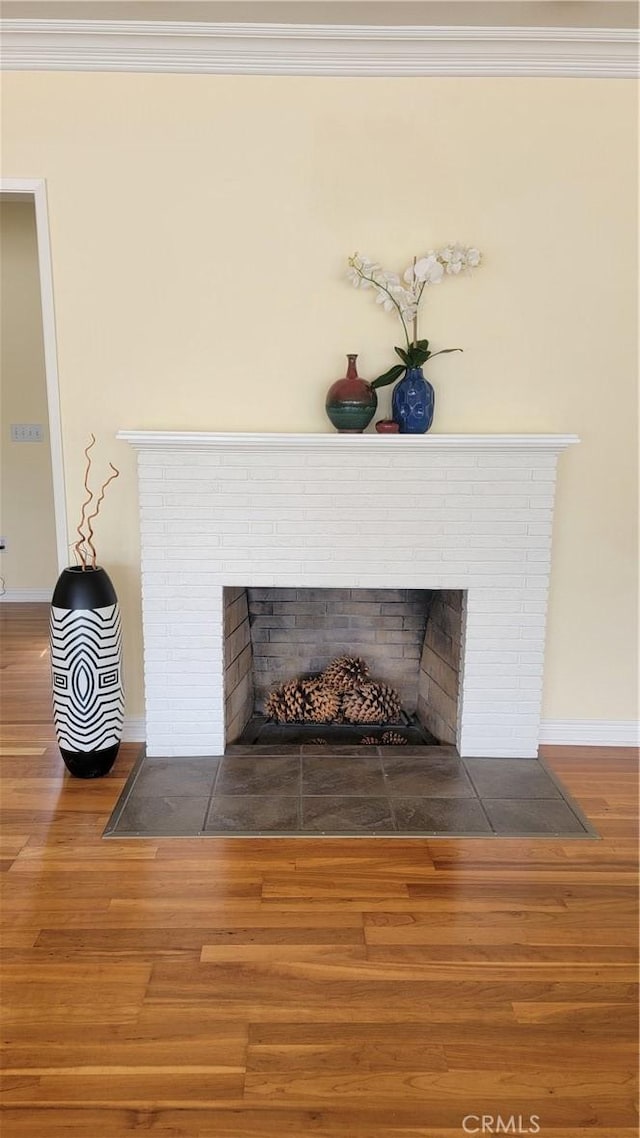 room details featuring a brick fireplace, crown molding, baseboards, and wood finished floors