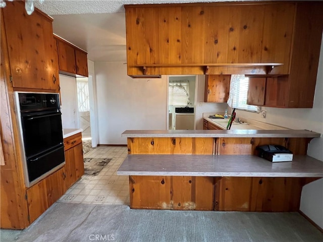 kitchen featuring a warming drawer, light countertops, brown cabinetry, a sink, and a peninsula