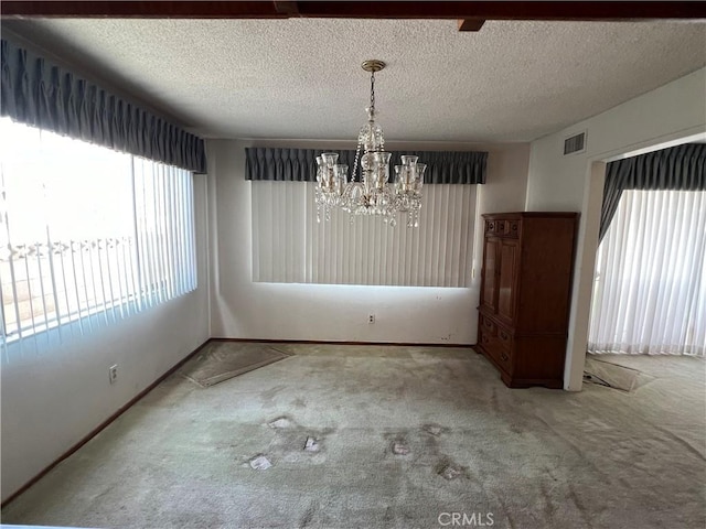 unfurnished dining area featuring carpet, visible vents, a notable chandelier, and a textured ceiling