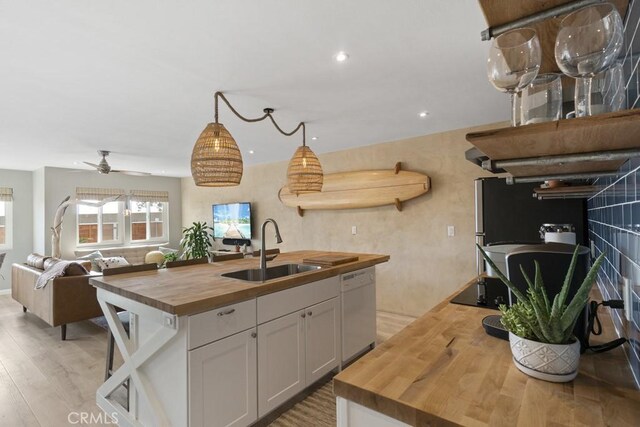 kitchen with light wood finished floors, wooden counters, open floor plan, white dishwasher, and a sink