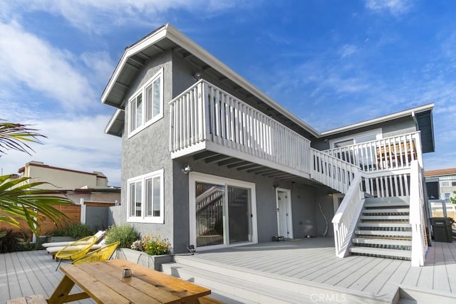 rear view of house with outdoor dining area, stairway, a deck, and stucco siding