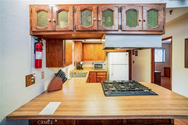 kitchen with glass insert cabinets, light countertops, a peninsula, white appliances, and a sink