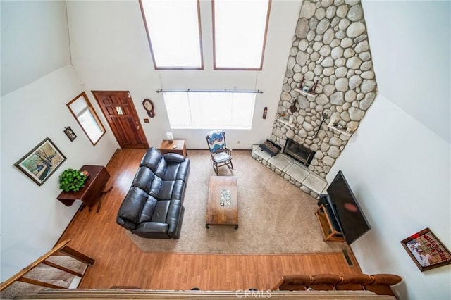 living room featuring a high ceiling, a stone fireplace, and wood finished floors