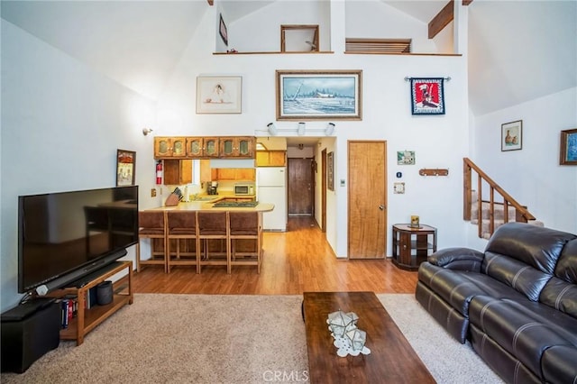 living area with high vaulted ceiling, stairs, and light wood finished floors