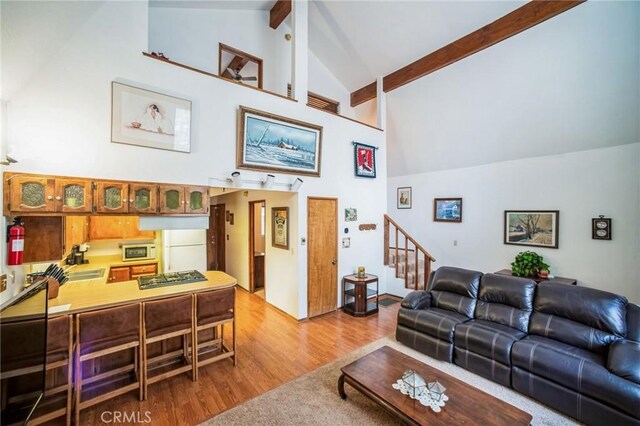 living area featuring stairway, beam ceiling, high vaulted ceiling, and light wood-style flooring