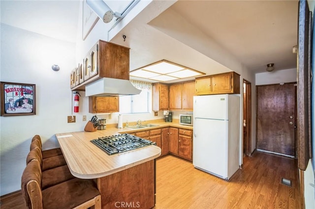 kitchen featuring a peninsula, freestanding refrigerator, a sink, light countertops, and light wood-type flooring